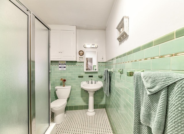 bathroom with toilet, a shower with shower door, and tile walls