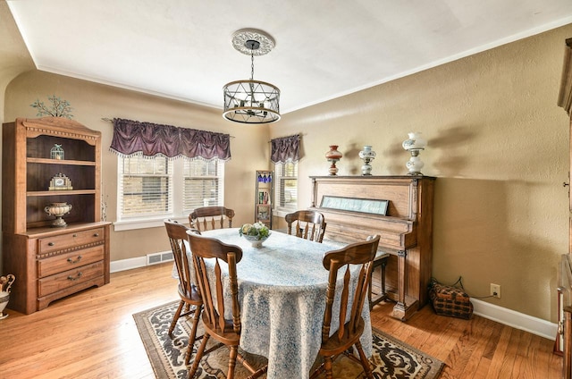 dining area featuring a notable chandelier, ornamental molding, and light hardwood / wood-style flooring