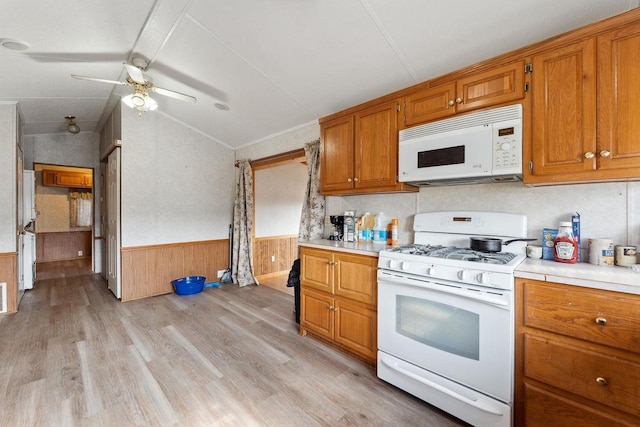 kitchen with white appliances, ceiling fan, lofted ceiling, wooden walls, and light hardwood / wood-style flooring