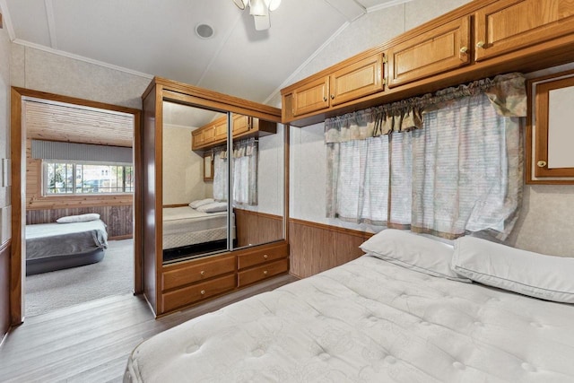 bedroom featuring lofted ceiling, ceiling fan, light wood-type flooring, a closet, and wooden walls