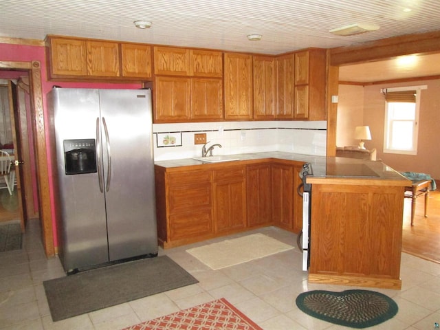 kitchen with tasteful backsplash, sink, light tile patterned flooring, kitchen peninsula, and stainless steel fridge