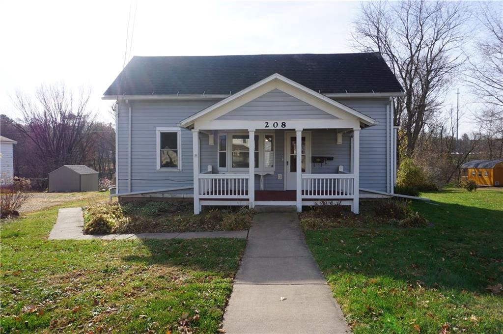 bungalow-style house featuring covered porch, a storage unit, and a front lawn