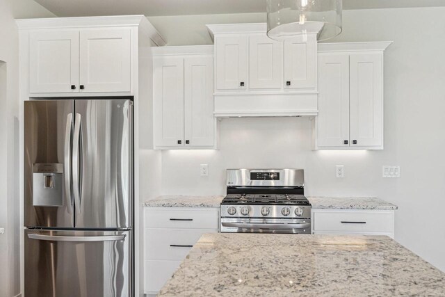 kitchen with light stone countertops, premium range hood, white cabinets, and stainless steel appliances