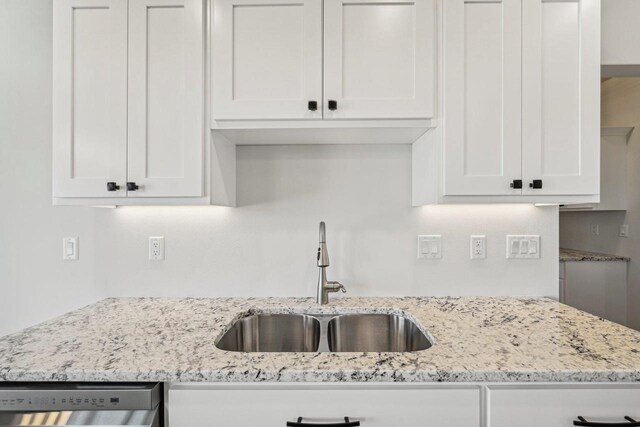 kitchen featuring stainless steel dishwasher, sink, white cabinets, and light stone countertops