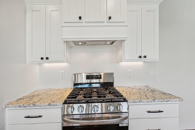 kitchen featuring stainless steel range with gas stovetop, light stone counters, white cabinets, and custom range hood