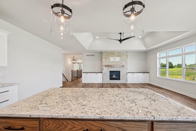 kitchen with white cabinetry, a tray ceiling, light wood-type flooring, a stone fireplace, and decorative light fixtures