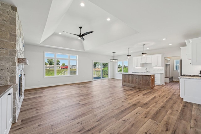 unfurnished living room featuring ceiling fan, a tray ceiling, light wood-type flooring, a stone fireplace, and sink