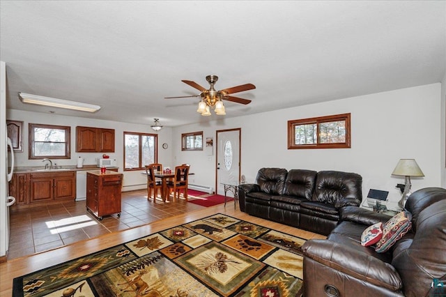 living room featuring baseboard heating, light tile patterned flooring, sink, and ceiling fan