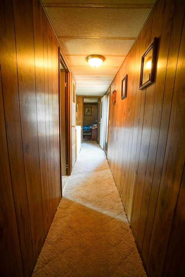 corridor featuring light carpet, a textured ceiling, and wooden walls