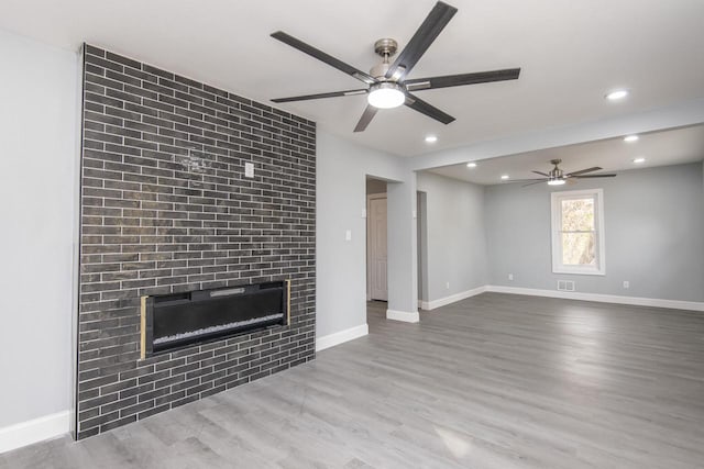 unfurnished living room with a large fireplace, light wood-type flooring, and ceiling fan