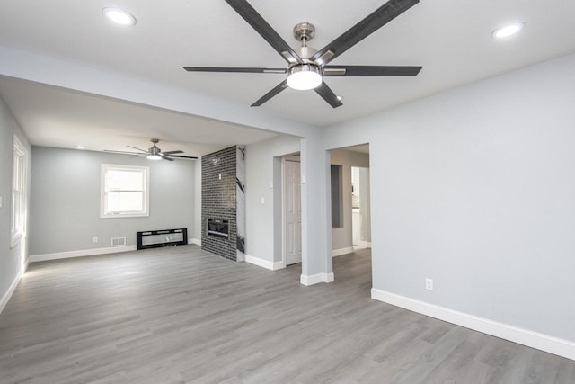 unfurnished living room featuring light hardwood / wood-style flooring, a brick fireplace, and ceiling fan