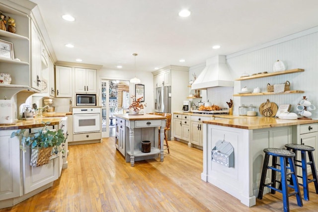 kitchen featuring butcher block counters, hanging light fixtures, a center island, white cabinetry, and appliances with stainless steel finishes