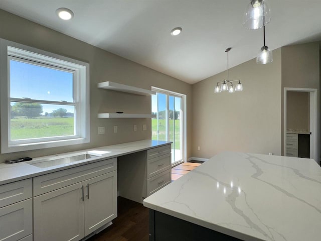 kitchen with a healthy amount of sunlight, light stone countertops, vaulted ceiling, and pendant lighting