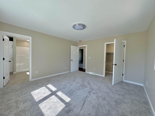 unfurnished bedroom with connected bathroom, light carpet, a closet, and a walk in closet