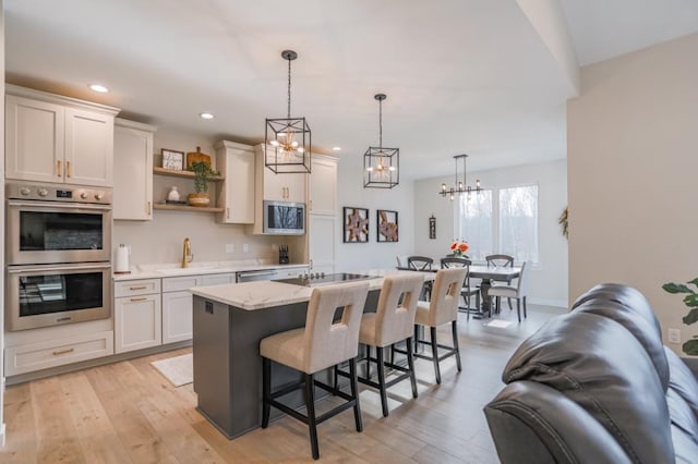 kitchen with stainless steel appliances, decorative light fixtures, an island with sink, and white cabinets