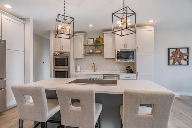 kitchen with appliances with stainless steel finishes, light hardwood / wood-style floors, pendant lighting, and an island with sink