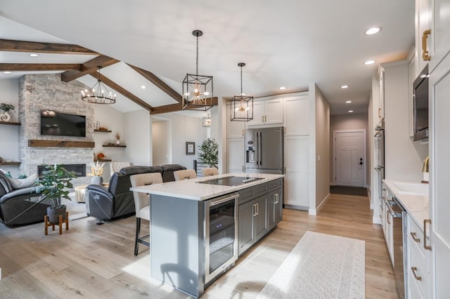 kitchen featuring an island with sink, stainless steel appliances, decorative light fixtures, white cabinets, and wine cooler