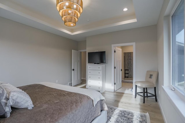 bedroom with connected bathroom, a raised ceiling, an inviting chandelier, and light wood-type flooring