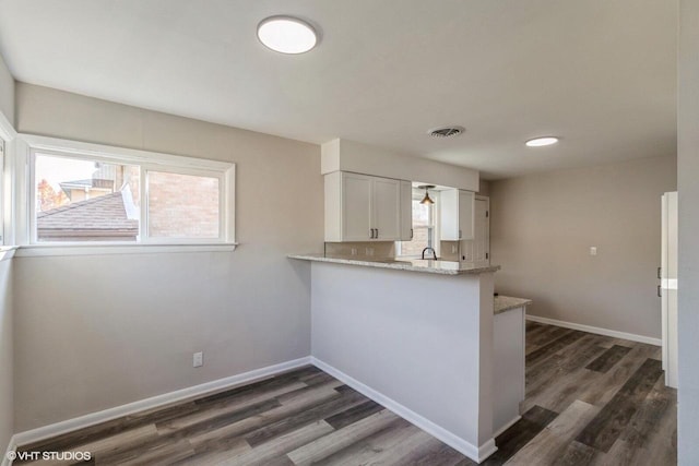 kitchen with kitchen peninsula, white cabinetry, dark wood-type flooring, sink, and light stone counters