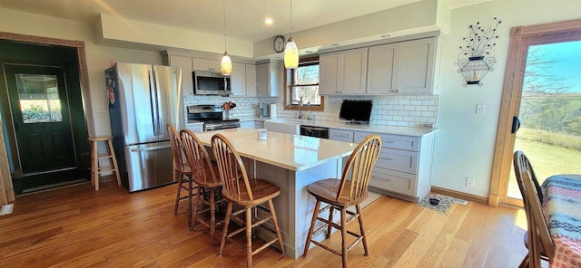 kitchen featuring light hardwood / wood-style flooring, a center island, decorative light fixtures, gray cabinets, and appliances with stainless steel finishes