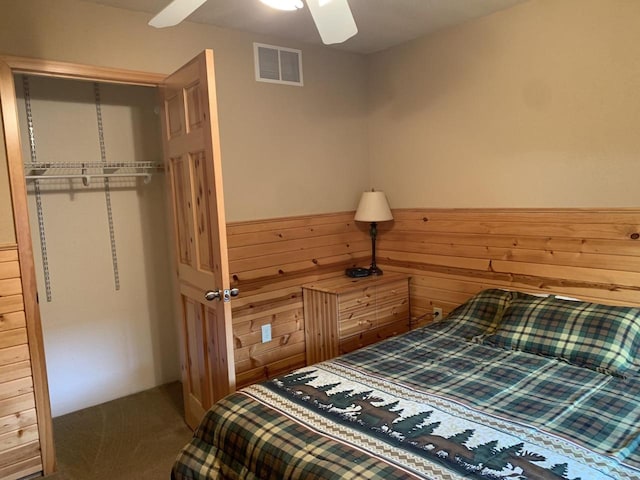 carpeted bedroom featuring a closet, ceiling fan, and wooden walls