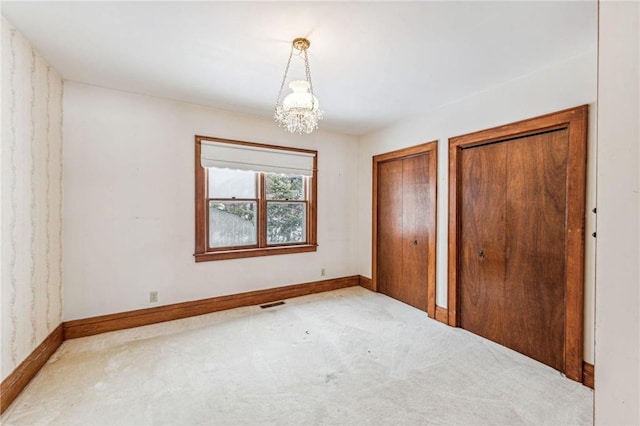 unfurnished bedroom with a notable chandelier, carpet flooring, and two closets