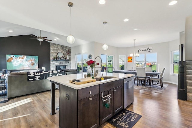 kitchen featuring a kitchen island with sink, stainless steel dishwasher, vaulted ceiling, a stone fireplace, and sink