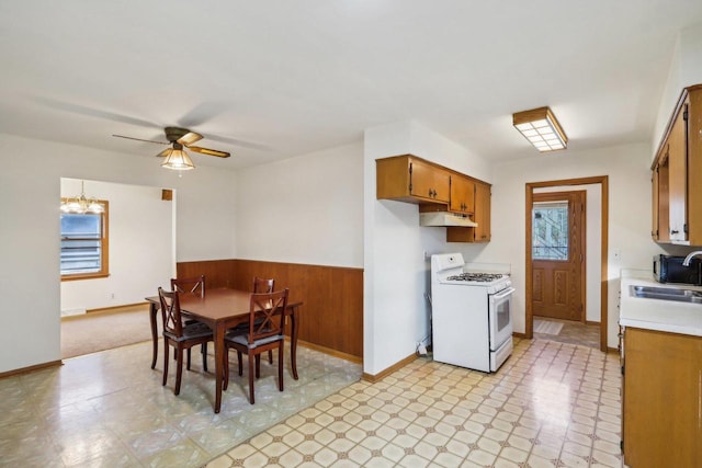 kitchen with ceiling fan, white gas stove, sink, and wooden walls