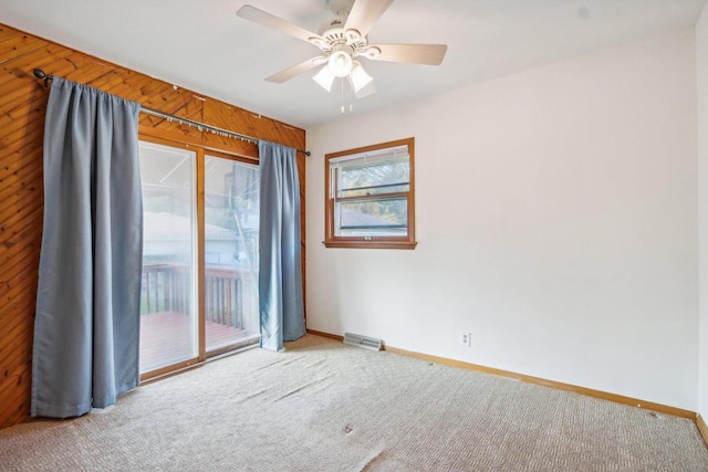 carpeted empty room with wooden walls and ceiling fan