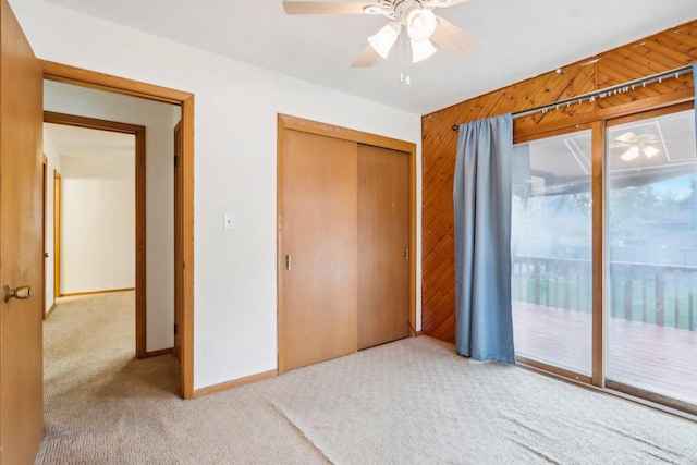 carpeted bedroom featuring a closet, ceiling fan, wooden walls, and access to exterior