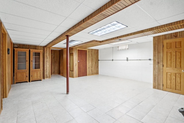 basement featuring wood walls and a drop ceiling