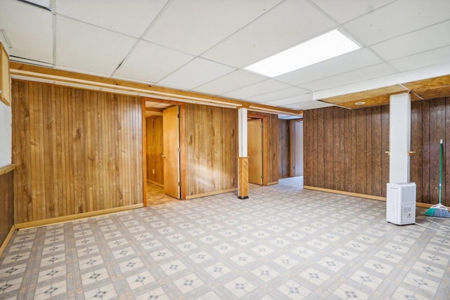 basement featuring a paneled ceiling and wooden walls