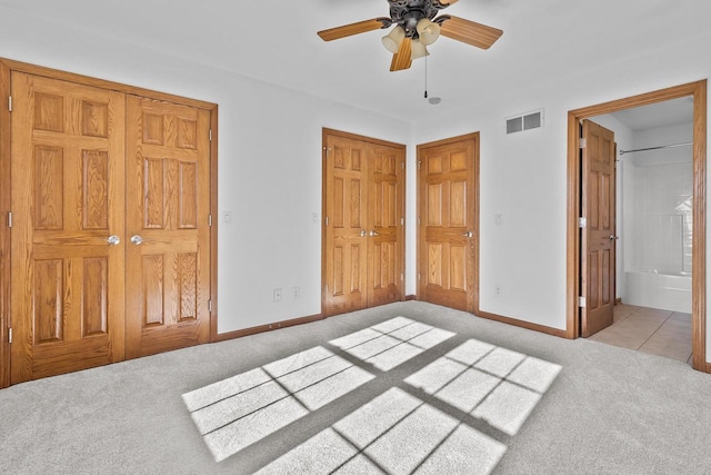 unfurnished bedroom featuring ensuite bath, two closets, ceiling fan, and light carpet