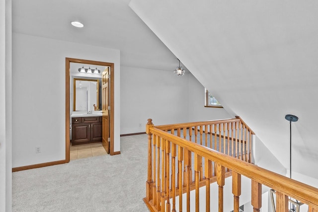 corridor featuring a notable chandelier, light colored carpet, vaulted ceiling, and sink