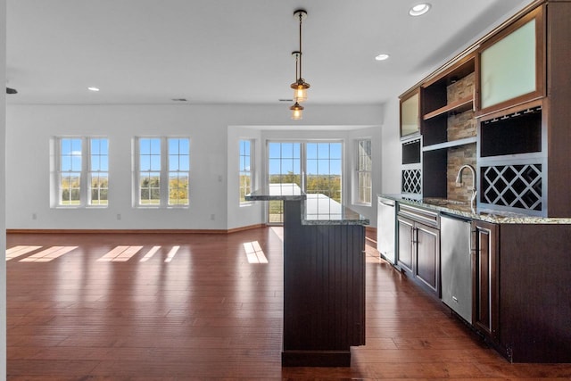 kitchen featuring dark wood-type flooring, decorative light fixtures, stainless steel dishwasher, and light stone countertops