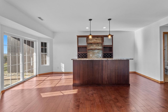 kitchen featuring light stone countertops, hanging light fixtures, and dark wood-type flooring