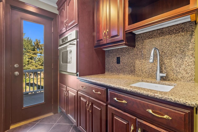 kitchen featuring dark tile patterned floors, stainless steel oven, backsplash, sink, and light stone counters