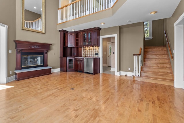 unfurnished living room with wine cooler, a high ceiling, light hardwood / wood-style flooring, and indoor bar