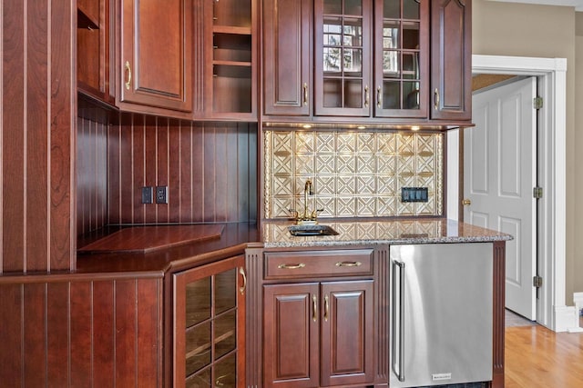 kitchen featuring stone counters, stainless steel fridge, light hardwood / wood-style flooring, and backsplash