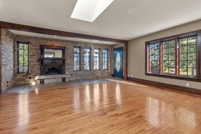 unfurnished living room featuring brick wall, light hardwood / wood-style flooring, and a skylight