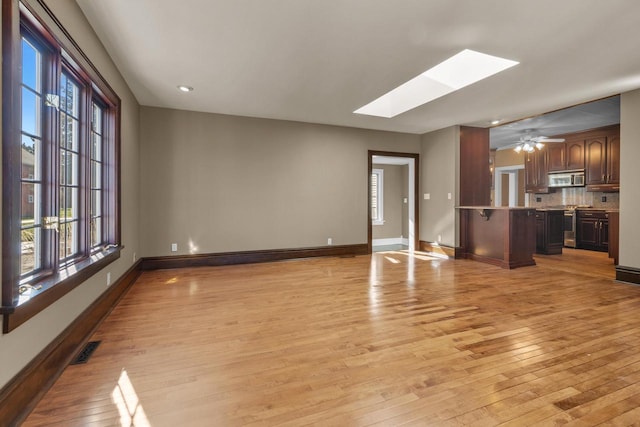 unfurnished living room featuring light hardwood / wood-style floors, a skylight, and a wealth of natural light