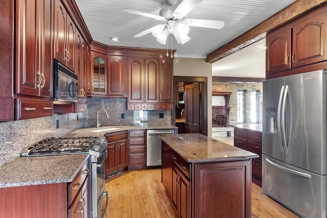 kitchen featuring sink, a center island, stainless steel appliances, dark stone counters, and light hardwood / wood-style flooring