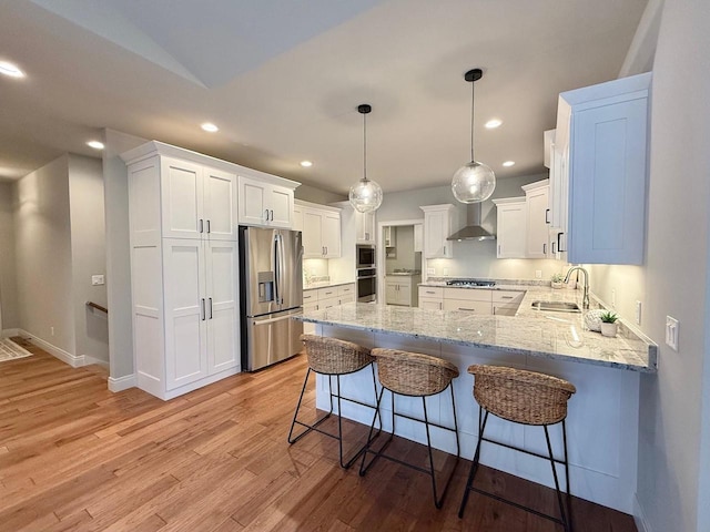 kitchen with appliances with stainless steel finishes, white cabinetry, wall chimney exhaust hood, pendant lighting, and light hardwood / wood-style flooring