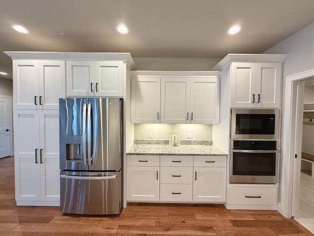 kitchen featuring appliances with stainless steel finishes, light hardwood / wood-style flooring, white cabinetry, and light stone counters