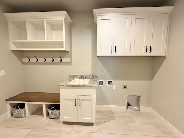 interior space with hookup for a washing machine, hookup for an electric dryer, sink, light tile patterned flooring, and cabinets