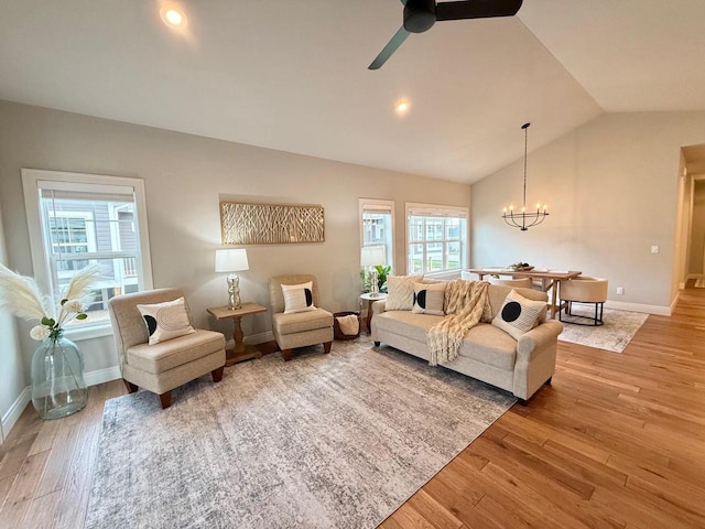 living room featuring wood-type flooring, ceiling fan with notable chandelier, and vaulted ceiling