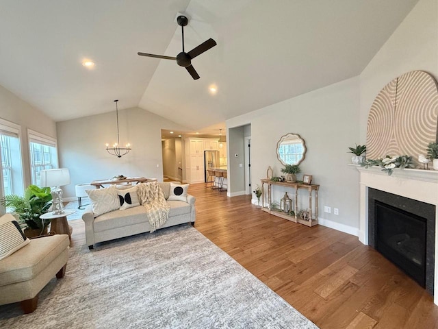 living room with hardwood / wood-style floors, vaulted ceiling, and ceiling fan with notable chandelier