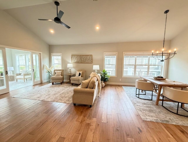 living room featuring high vaulted ceiling, ceiling fan with notable chandelier, and light wood-type flooring