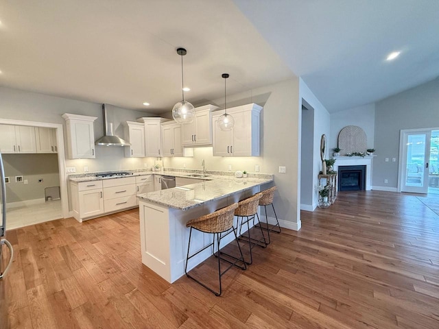 kitchen with wall chimney range hood, kitchen peninsula, white cabinetry, and sink