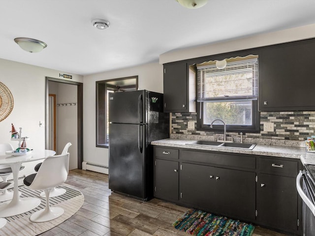 kitchen with wood-type flooring, a baseboard radiator, sink, black fridge, and decorative backsplash